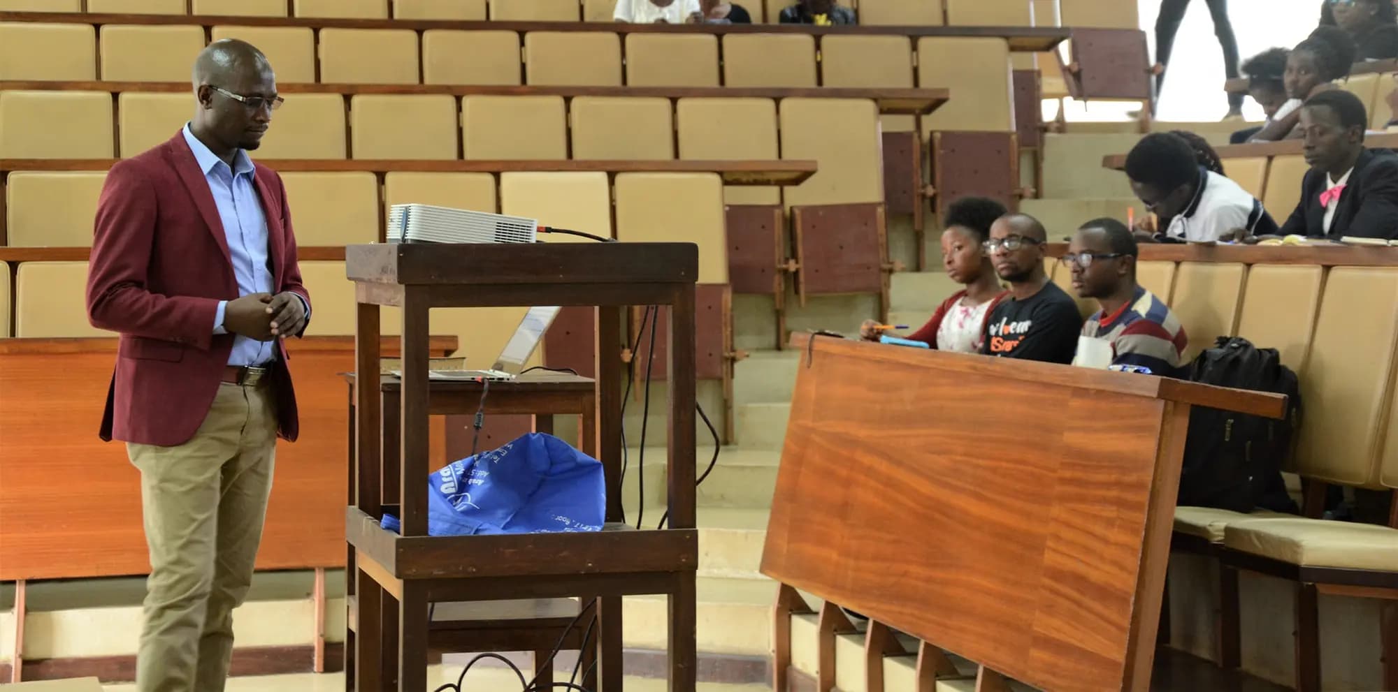 Teaching at a campus fellowship: a speaker beside a lectern in a lecture hall, students listening from the tiered benches
